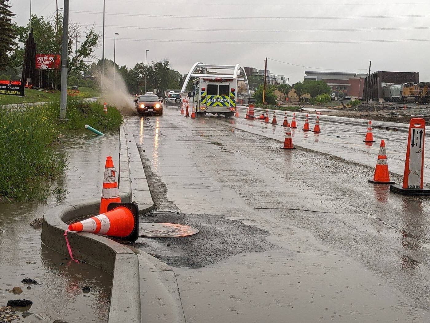 A car driving through a flooded city street, throwing up a wave of contaminated floodwater that hides health and physical hazards