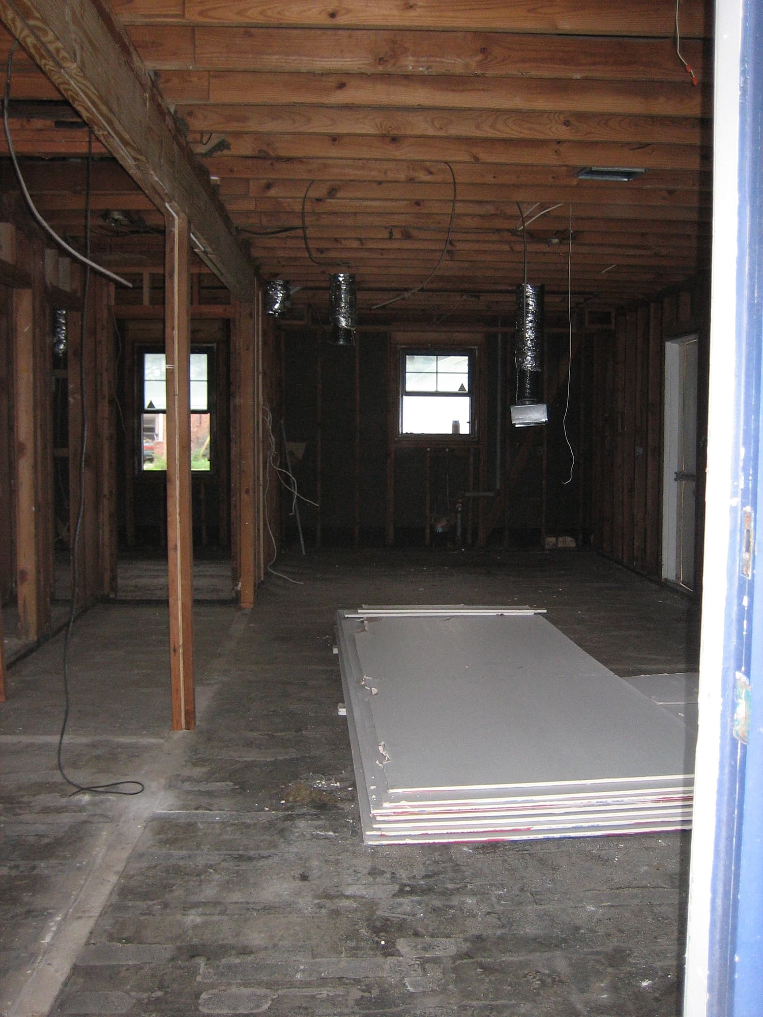 A flood-gutted house interior with wet drywall removed and piles of sheetrock awaiting disposal